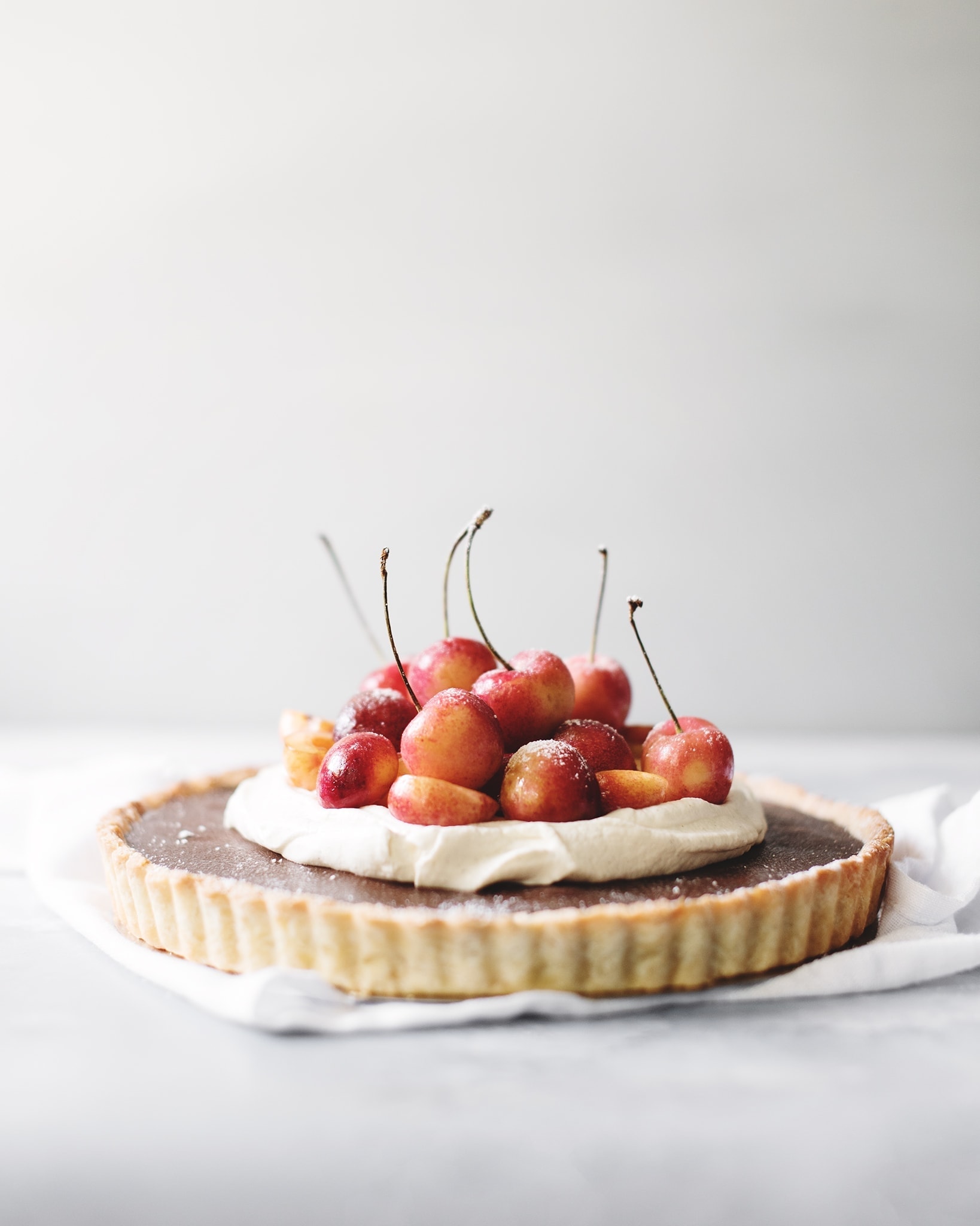 Rainier cherries on top of whipped cream and chocolate ganache tart on grey background