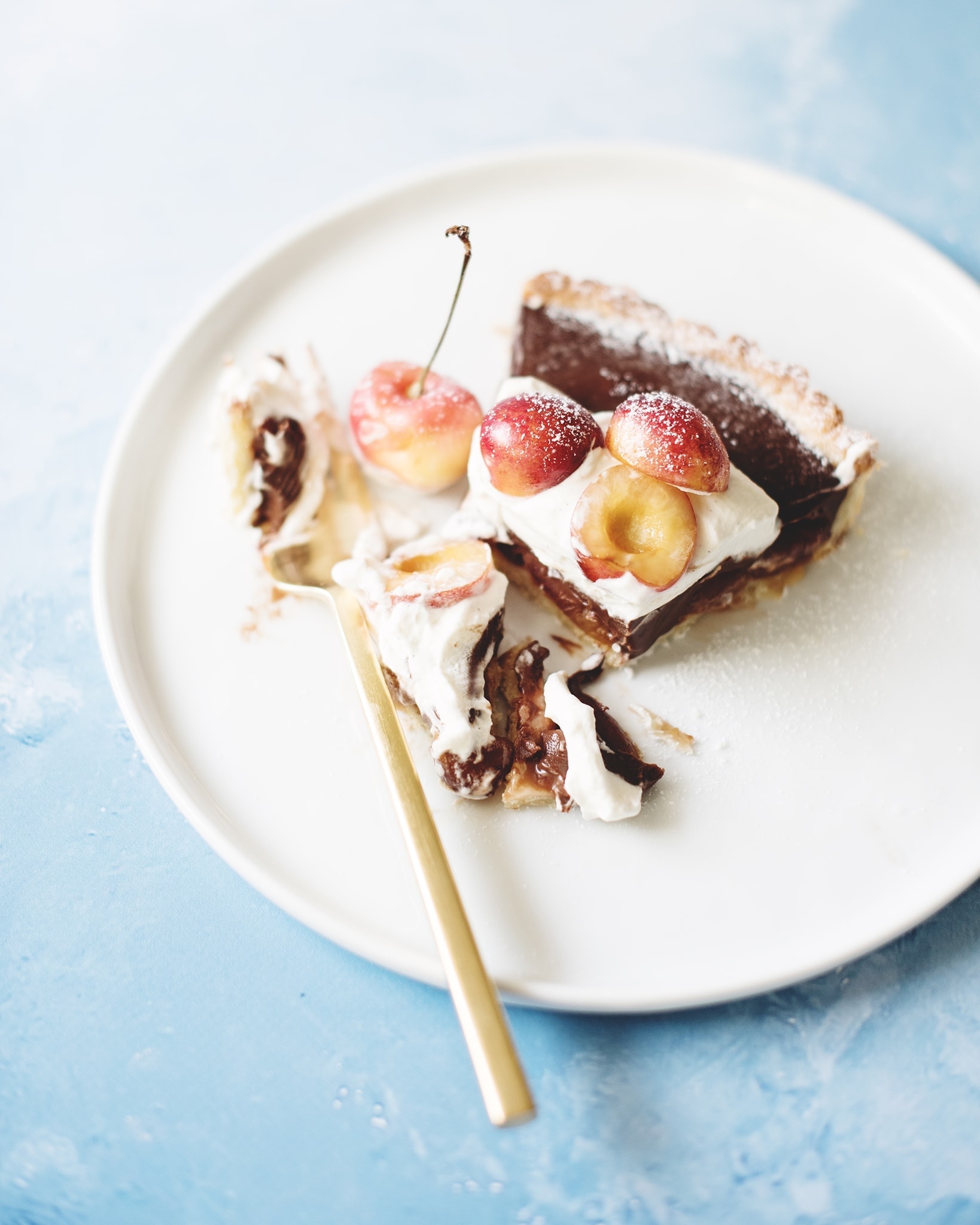 Fork cutting into a slice of chocolate cherry tart with cardamom cream on white plate