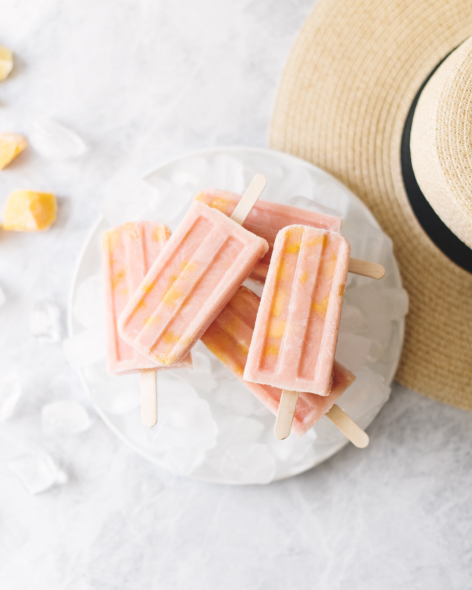 Stack of mango guava popsicles on top of plate of ice next to straw hat