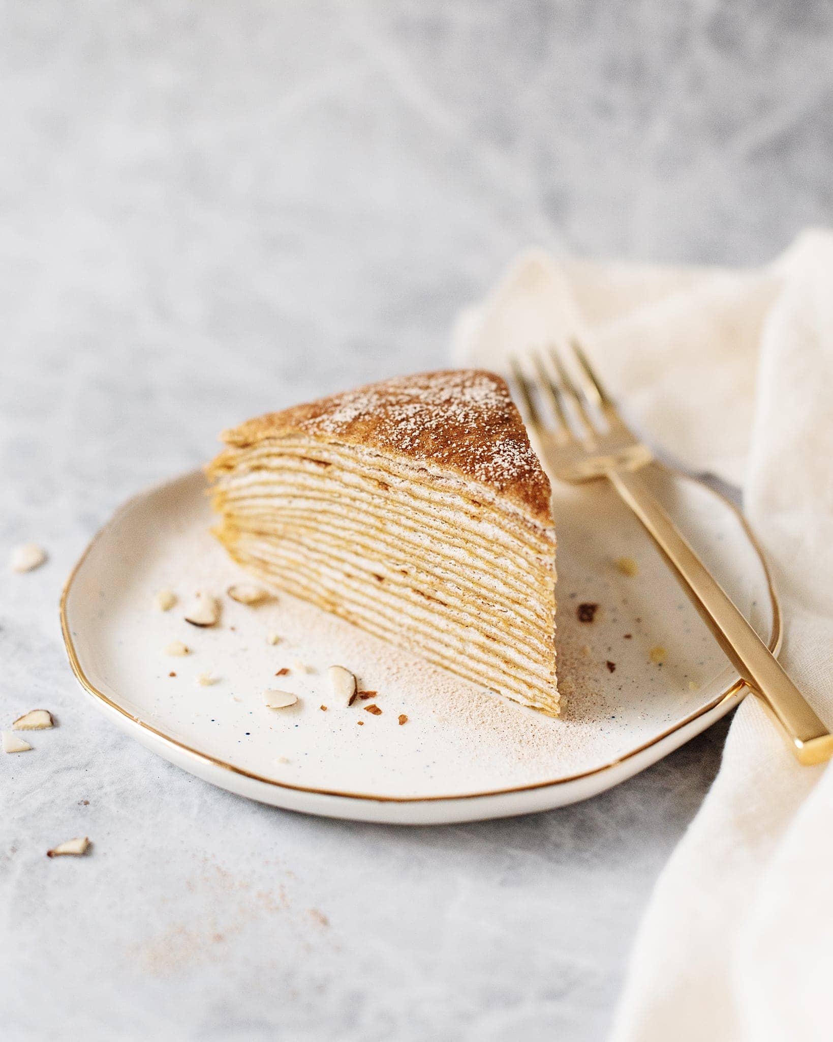 A slice of pumpkin crepe cake on a white gold-rimmed plate with a gold fork