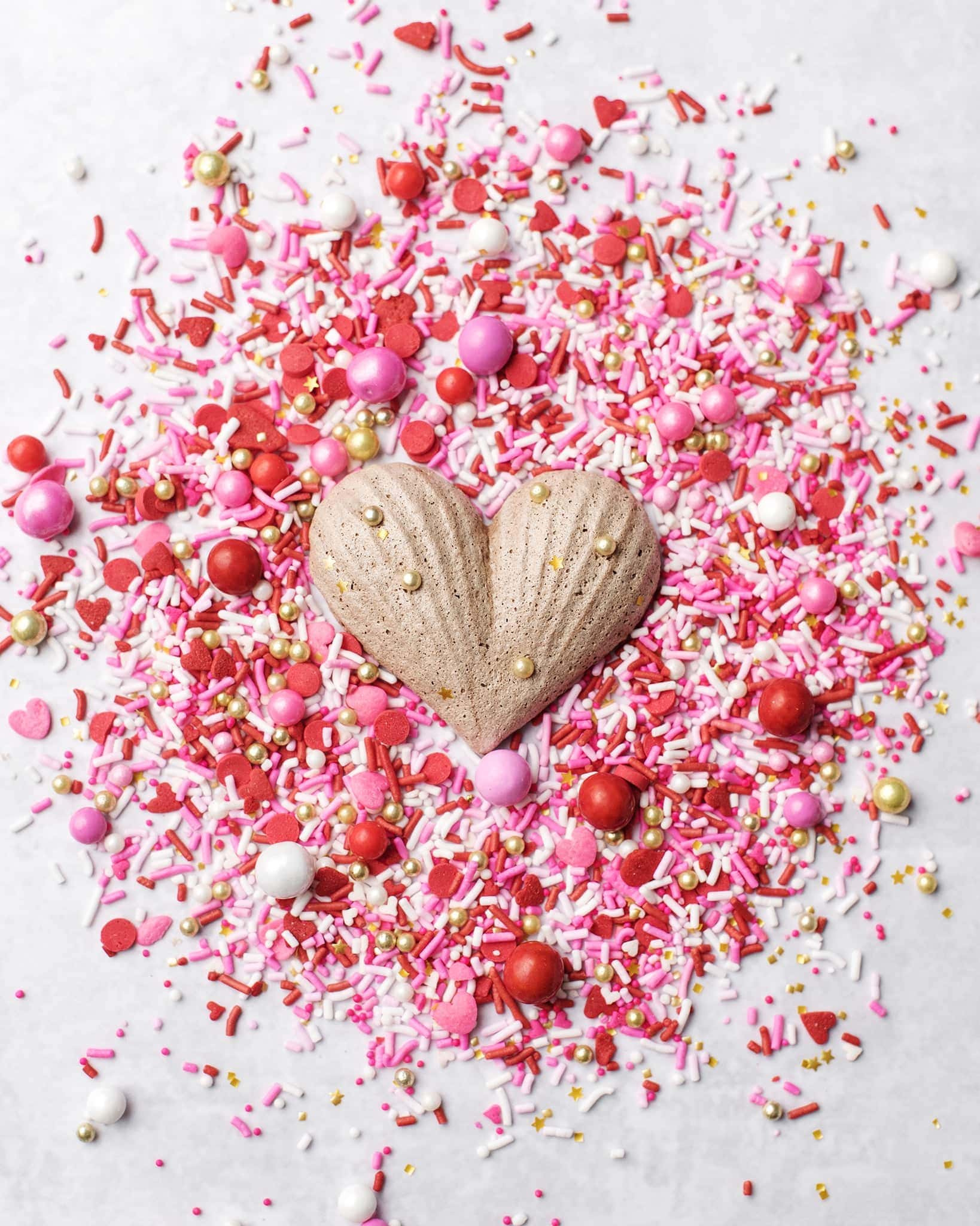 One chocolate meringue surrounded by pink, red, gold, and white sprinkles