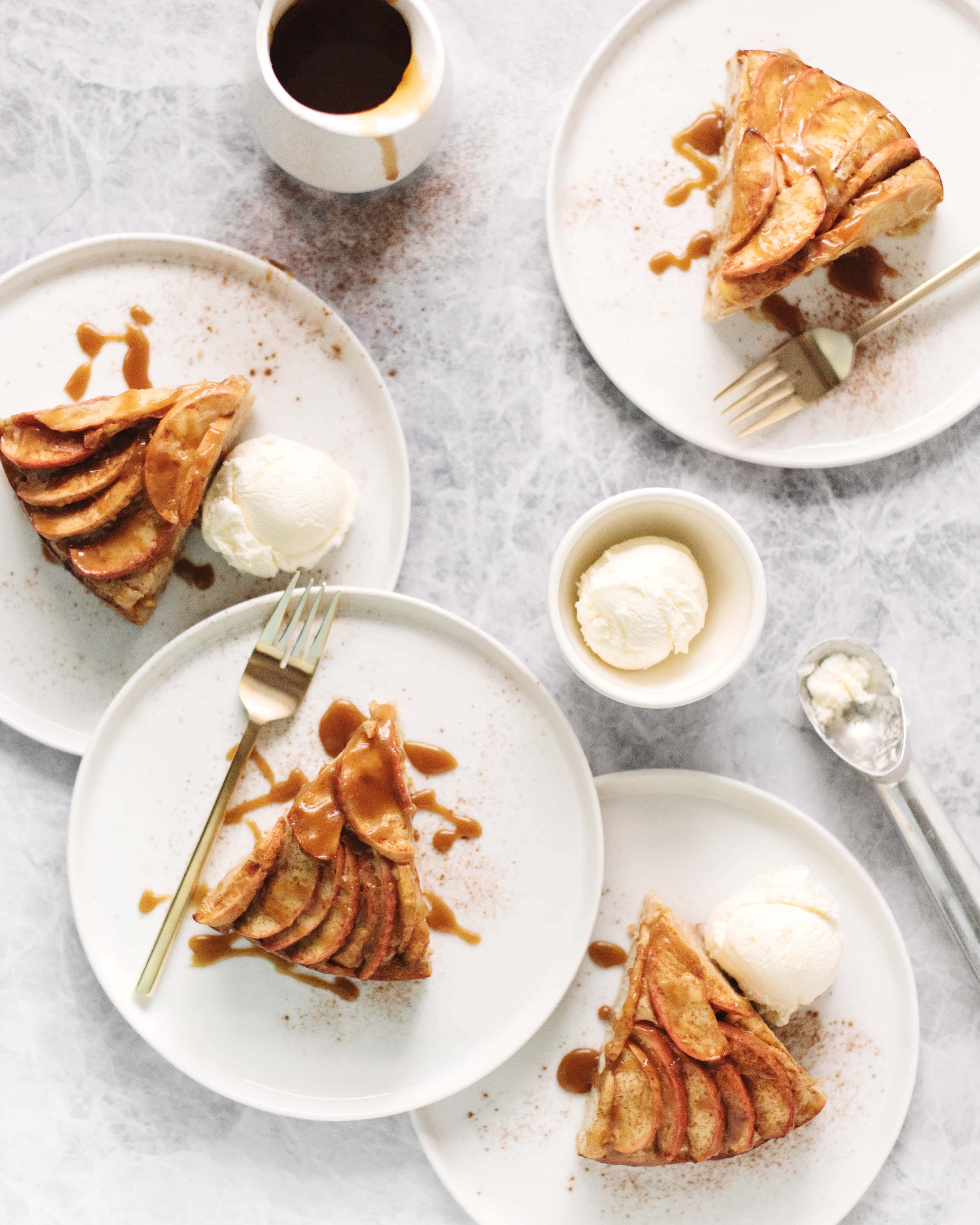 4 slices of spiced apple cake drizzled with salted maple caramel on white plates with scoops of vanilla ice cream