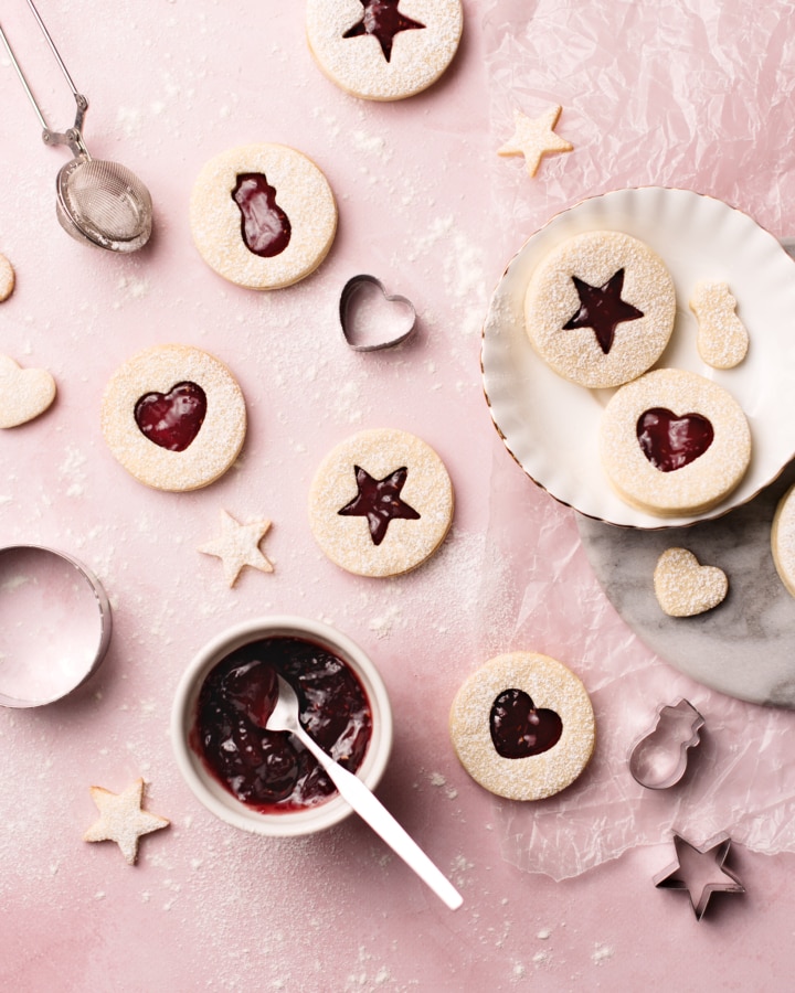 Raspberry rose linzer cookies with heart, star, and snowman cutouts on a pink background