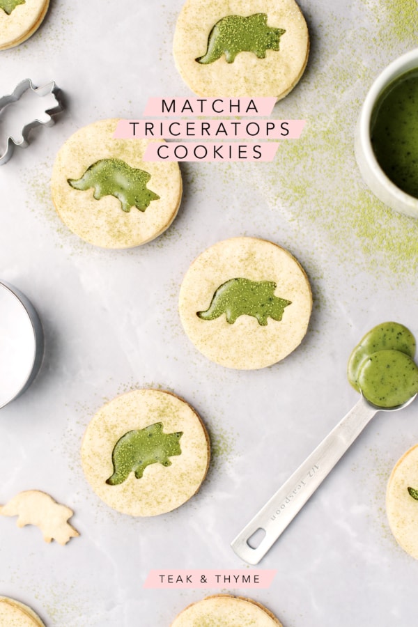 Matcha linzer cookies with triceratops cutouts on a grey background and sprinkled with matcha powder