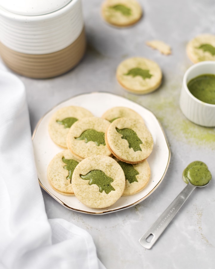 A plate of matcha linzer cookies next to a spoonful of matcha ganache
