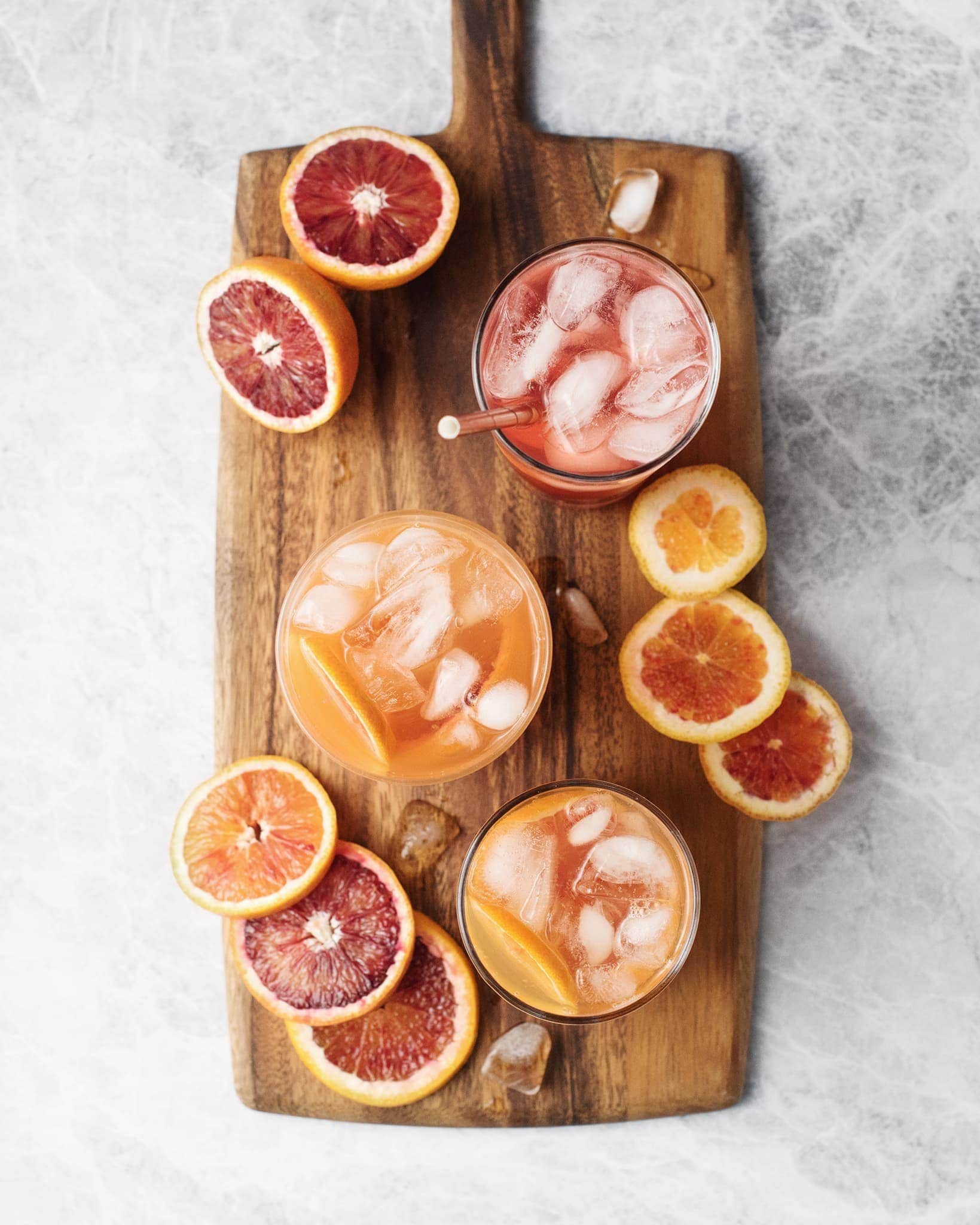 Glasses of blood orange palomas and blood orange slices on a wooden serving board
