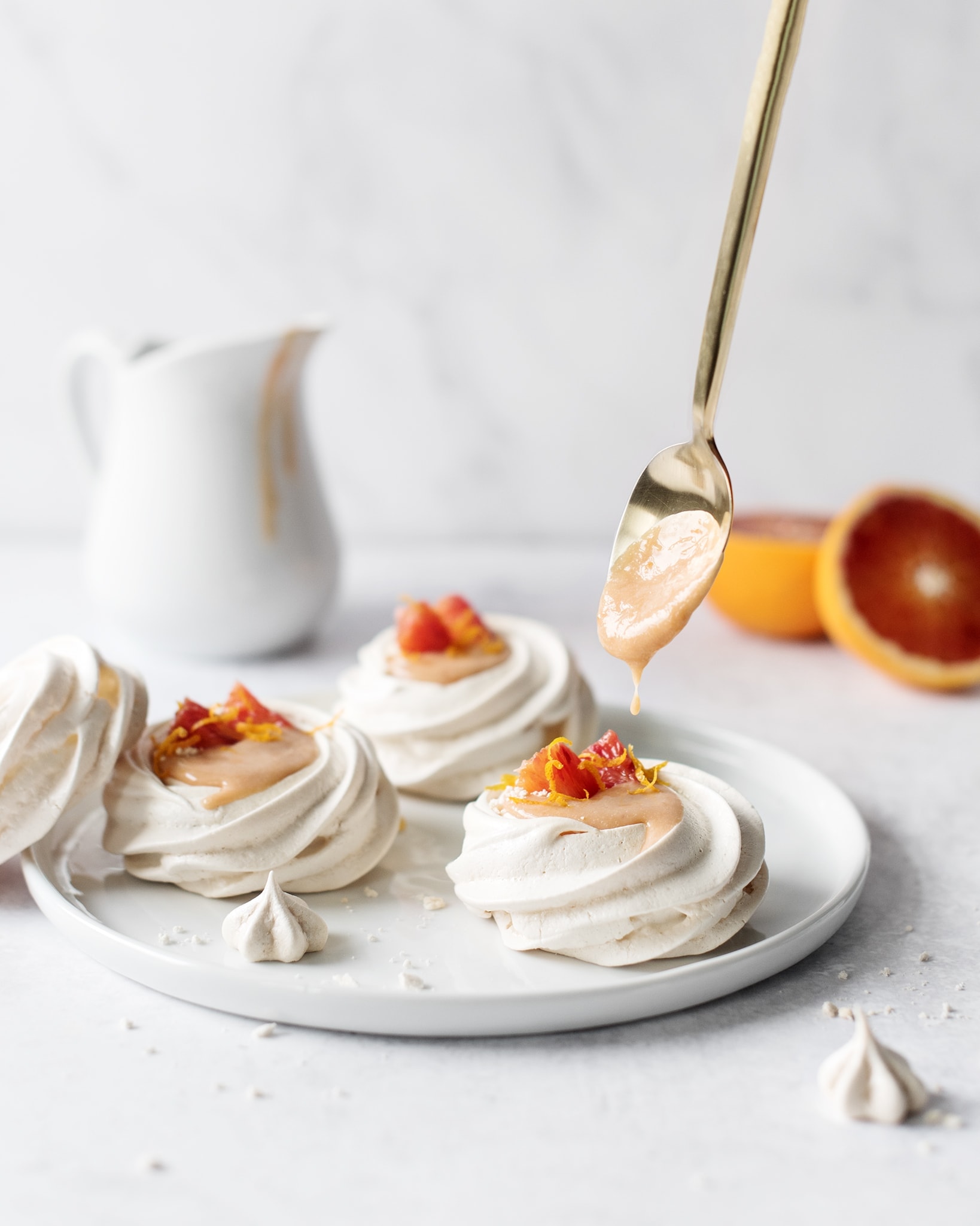 Spoonful of blood orange curd dripping into mini pavlovas