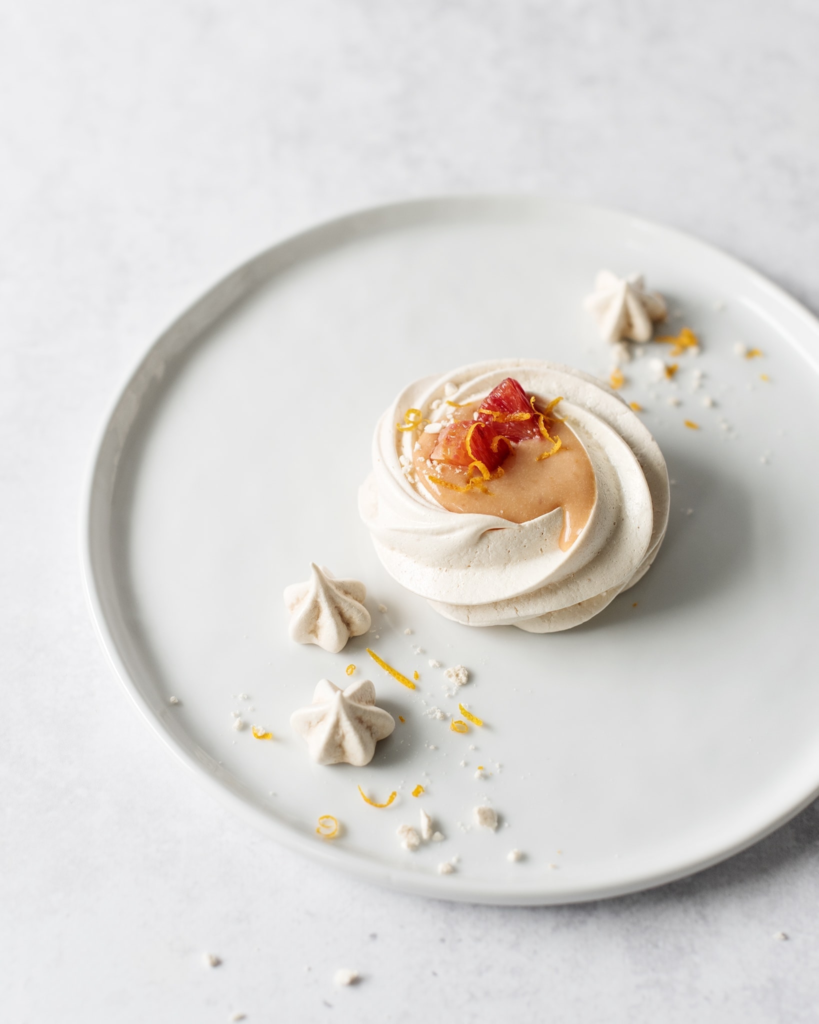 One blood orange pavlova on a white plate with mini meringues