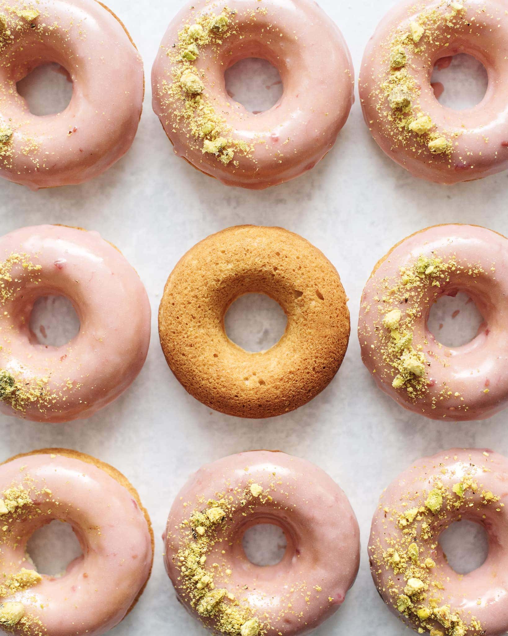 One unglazed donut surrounded by glazed raspberry pistachio donuts