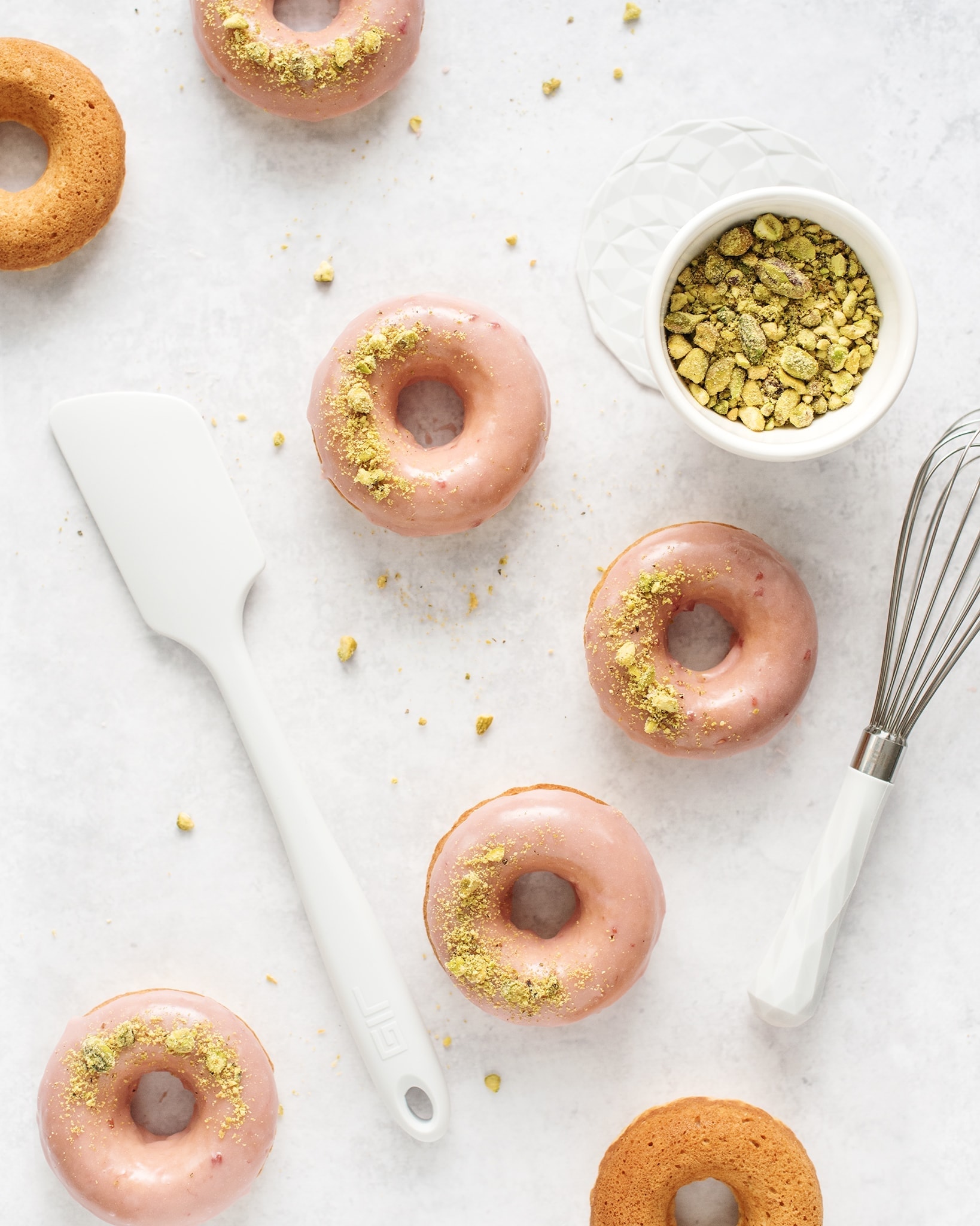 Raspberry pistachio donuts on a grey background with a spatula and whisk