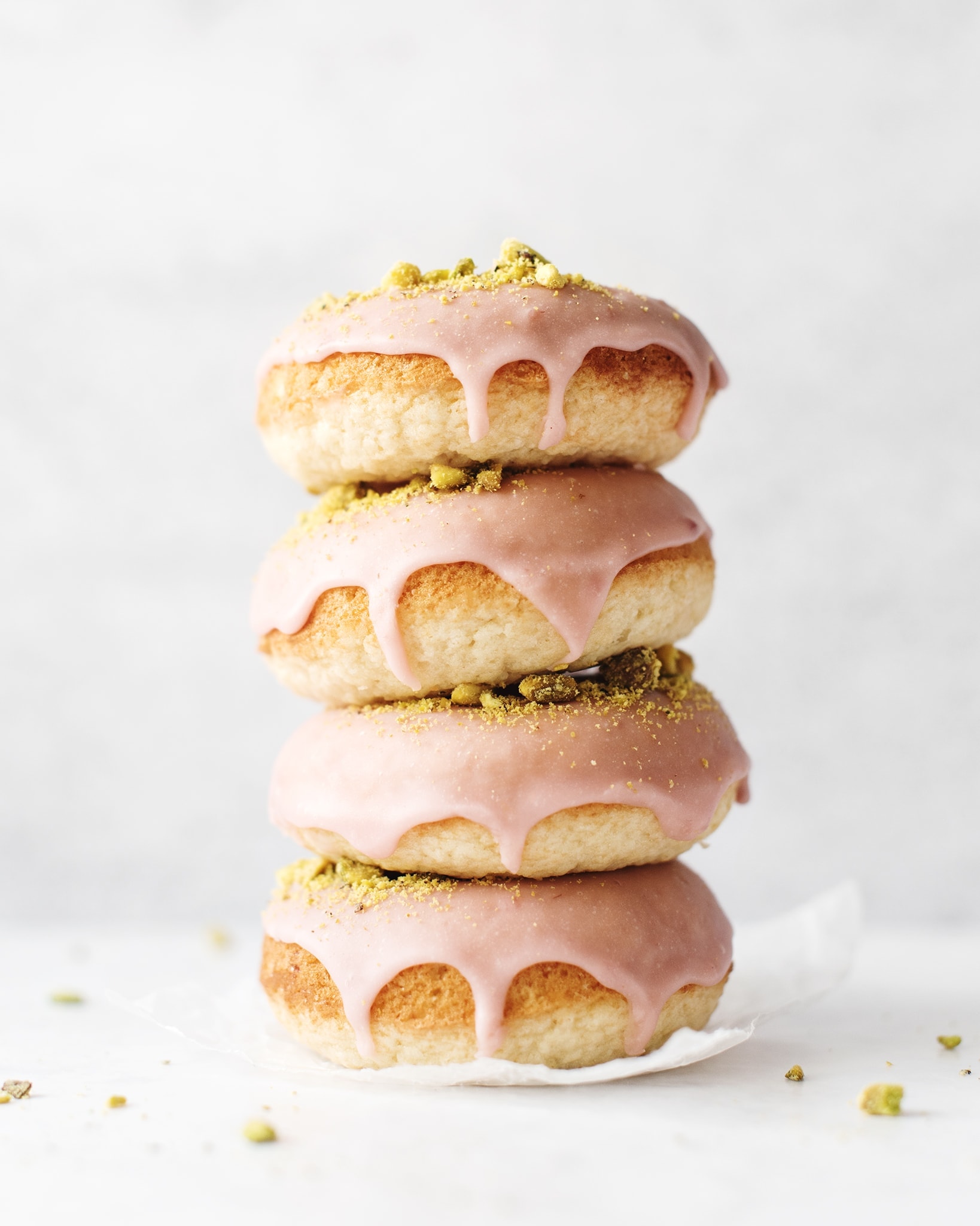 Stack of four raspberry pistachio donuts dripping with glaze