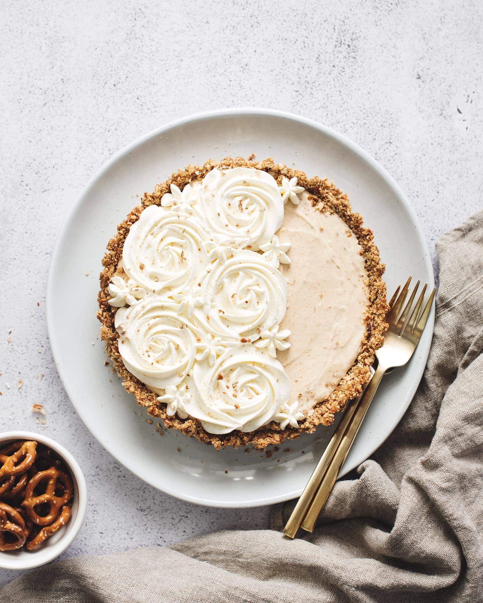 Peanut butter ice cream pie with whipped cream rosettes and brown linen and bowl of pretzels