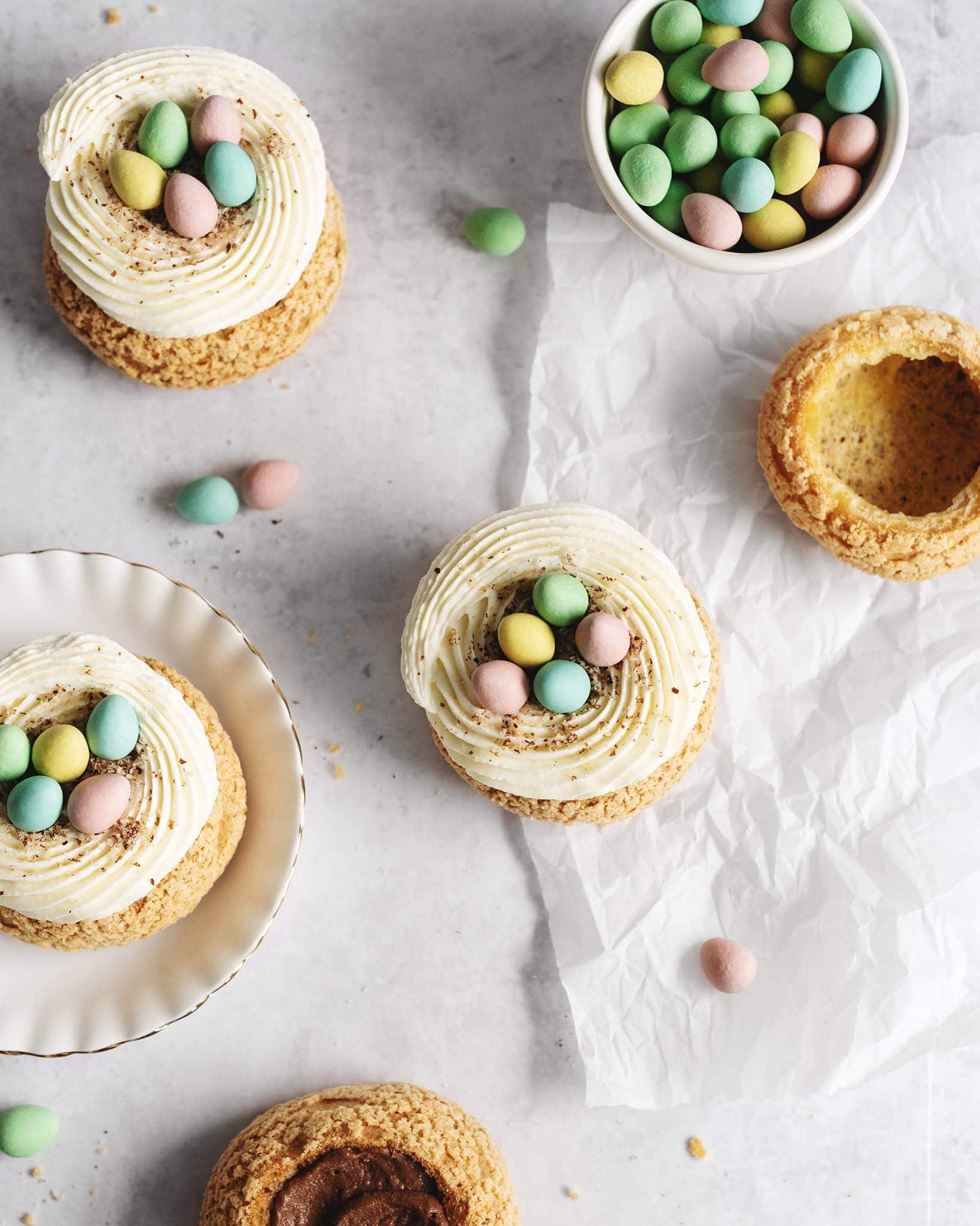 Overhead shot of cream puffs on parchment with a bowl of mini eggs
