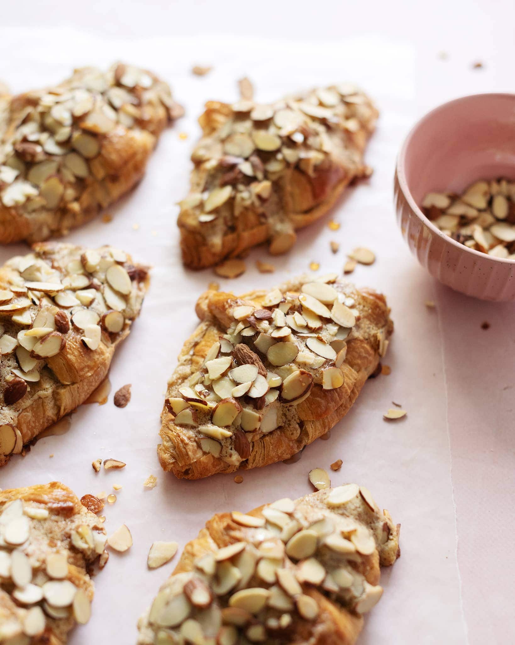 Almond croissants sprinkled with sliced almonds on pink background