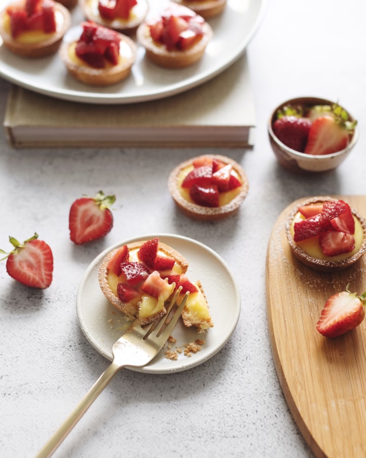 Fork cutting into a lemon curd tartlet topped with strawberries