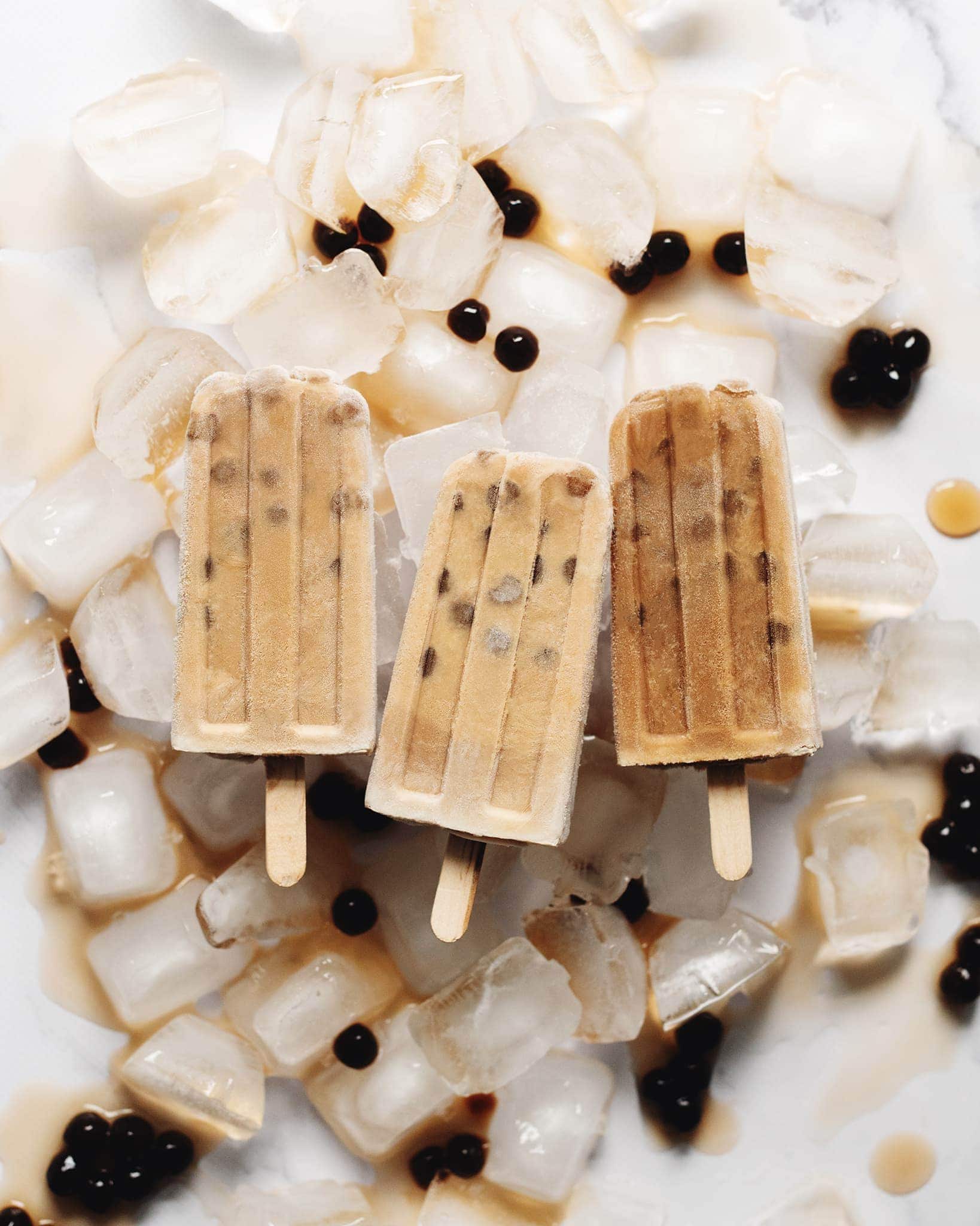 Boba milk tea popsicles on top of ice cubes surrounded by tapioca pearls