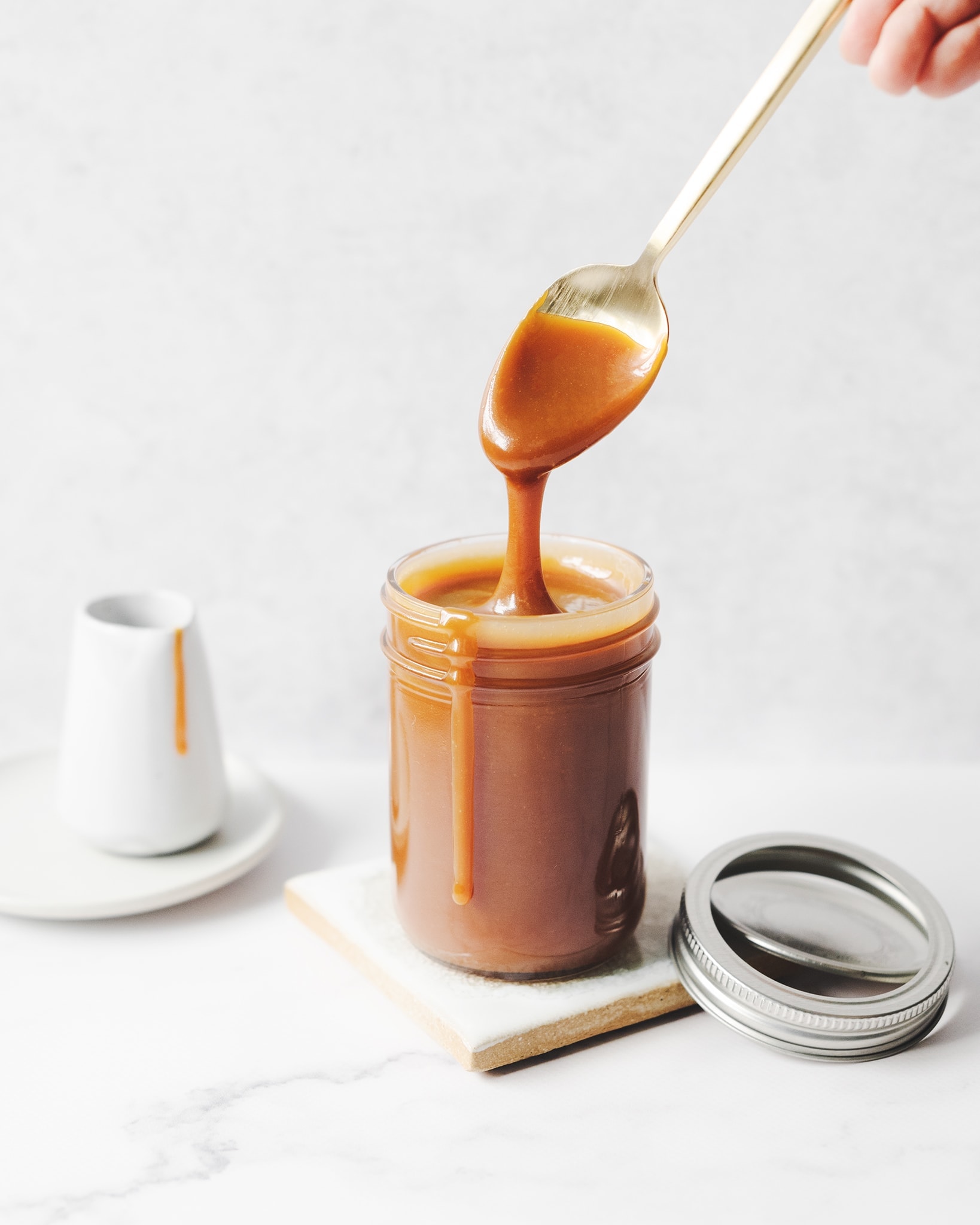 Spoon dripping with caramel sauce above glass jar