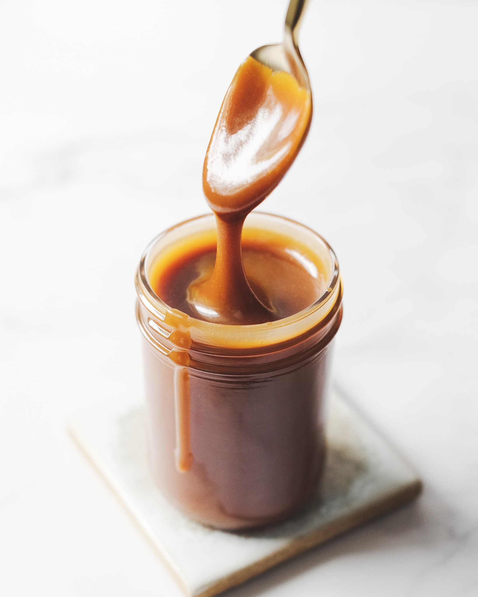 Spoon dripping with caramel sauce above glass jar
