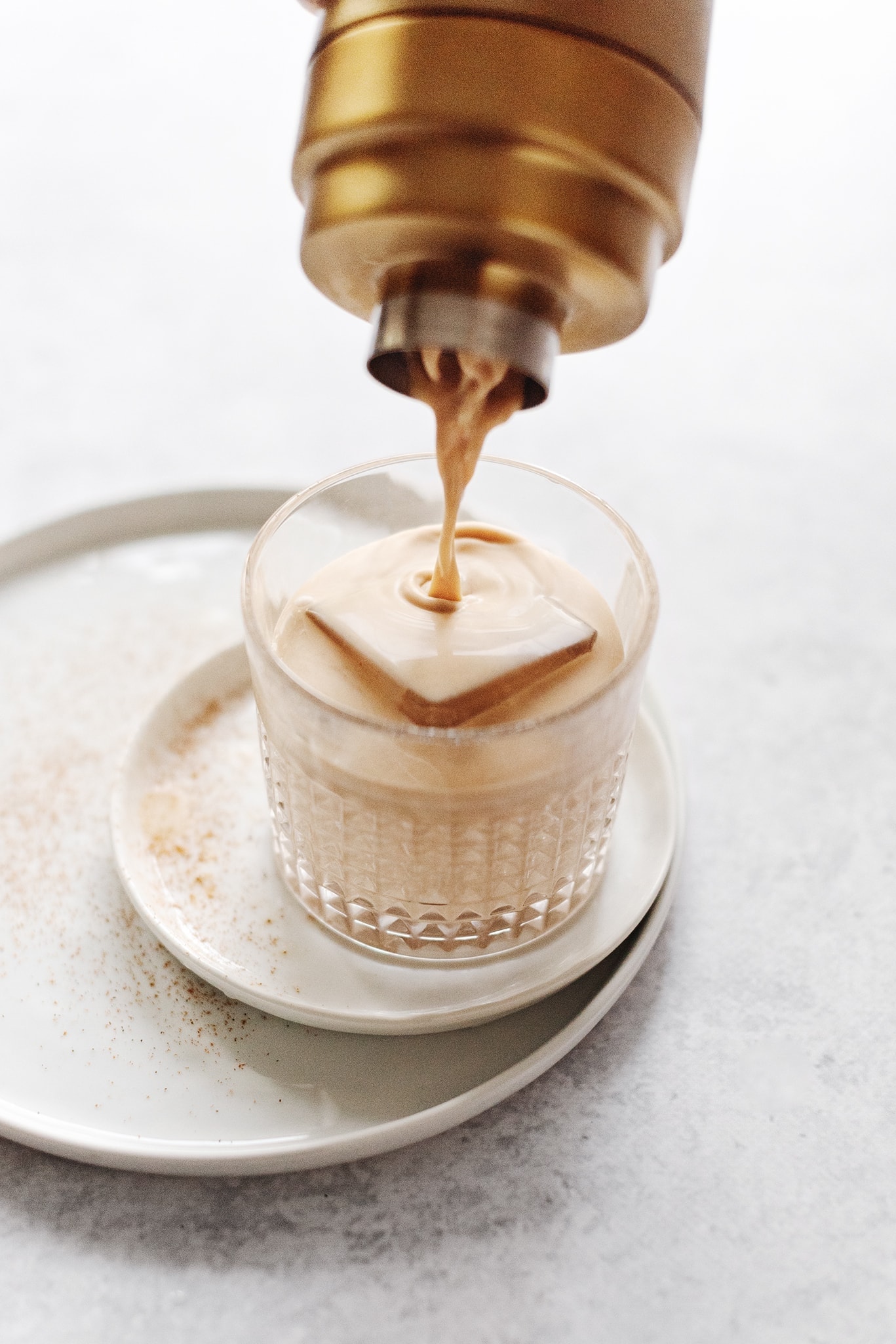 Pouring a pumpkin spice white russian cocktail from gold shaker into glass
