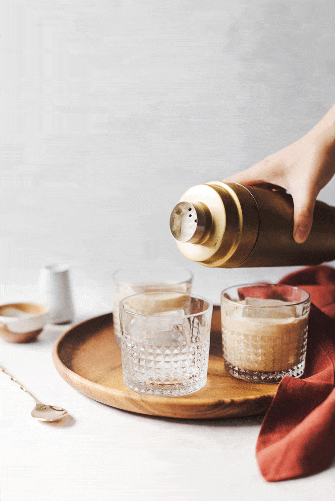 Pouring a pumpkin spice white russian cocktail from gold shaker into glasses