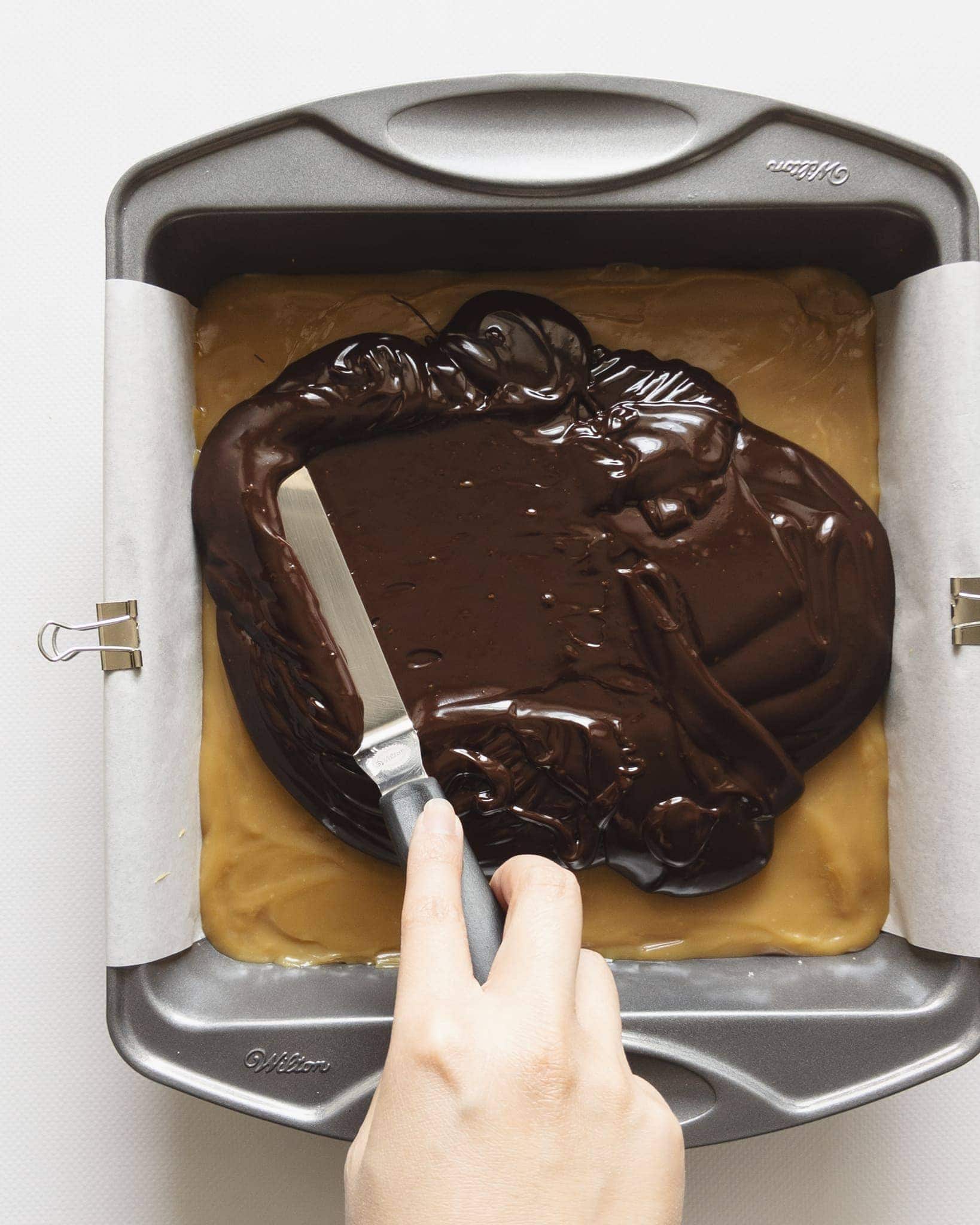 Spreading chocolate ganache across caramel layer