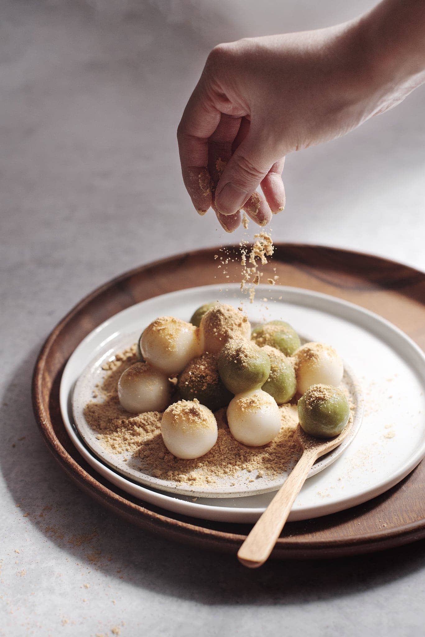 Hand sprinkling kinako on top of pile of dango