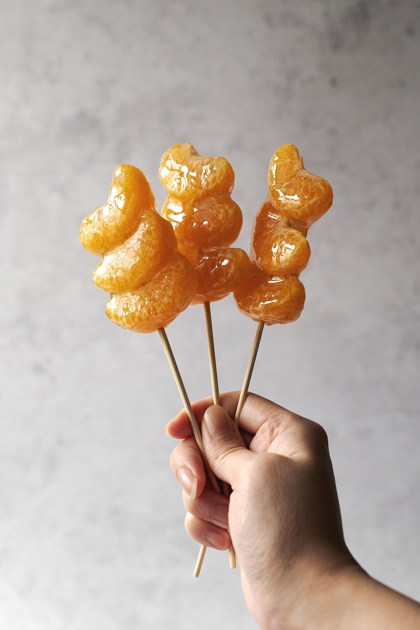 Hand holding skewers of tangerine tanghulu