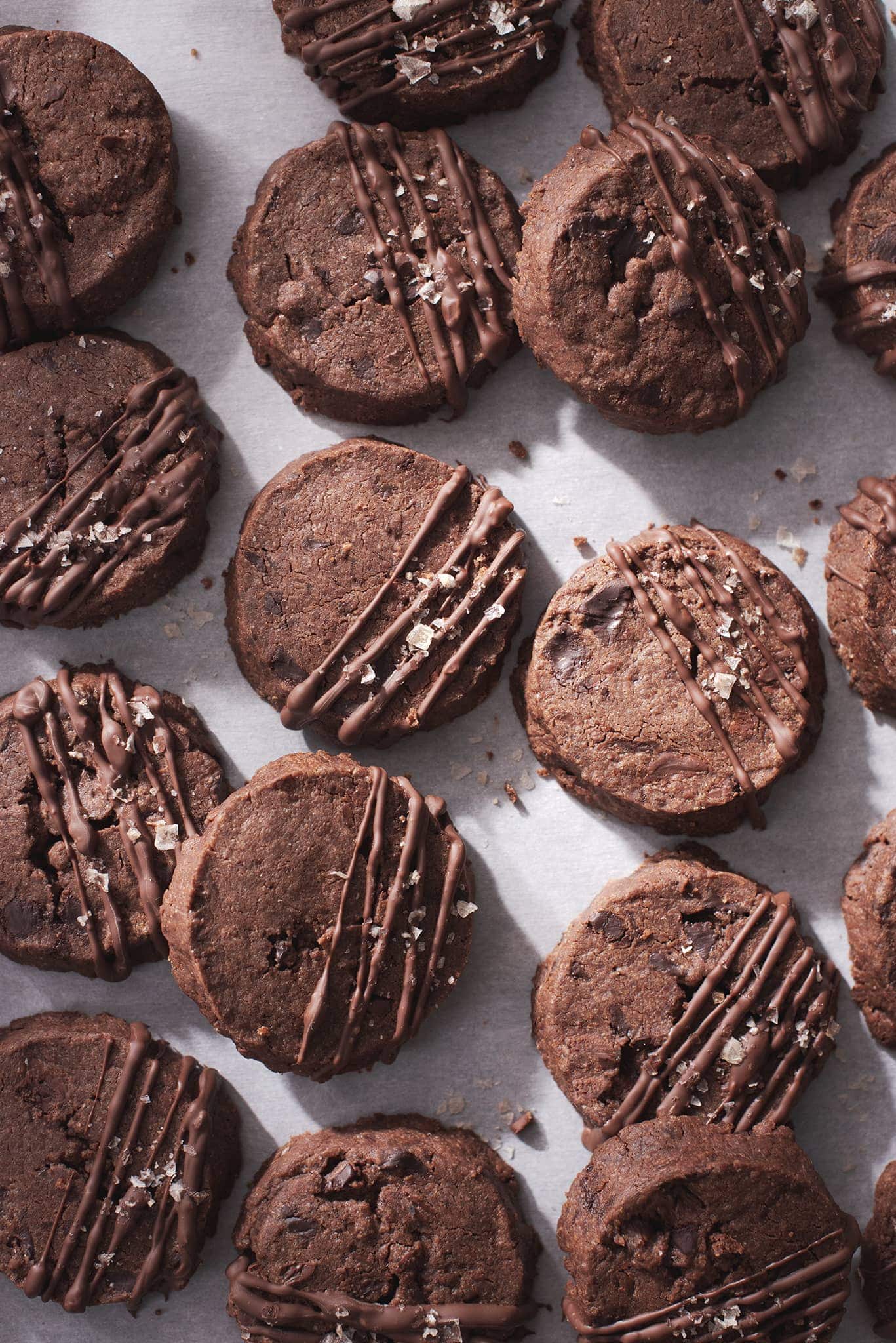 Many chocolate sablé cookies on scattered on baking sheet