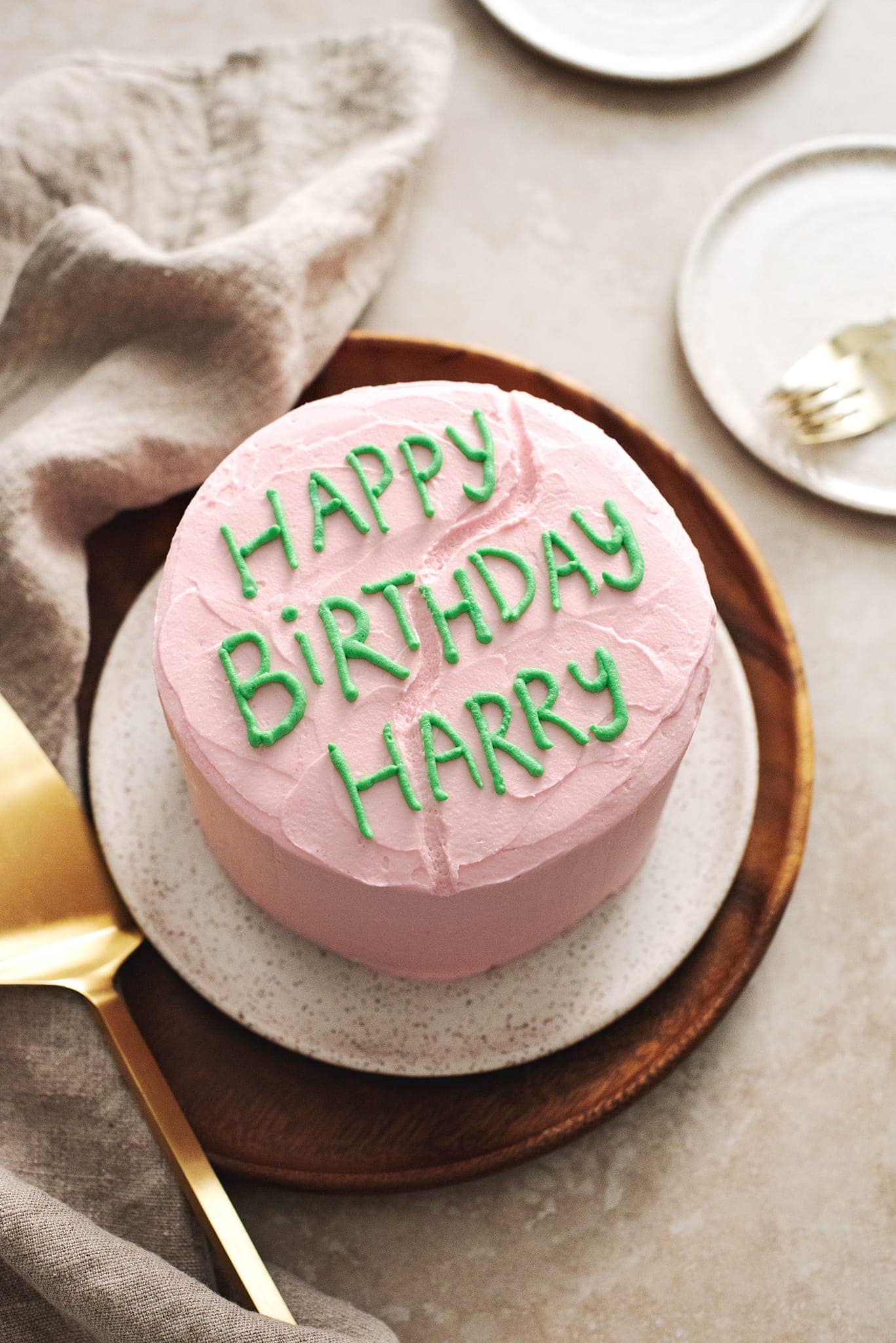 Pink cake with โHappy Birthday Harryโ written in green icing