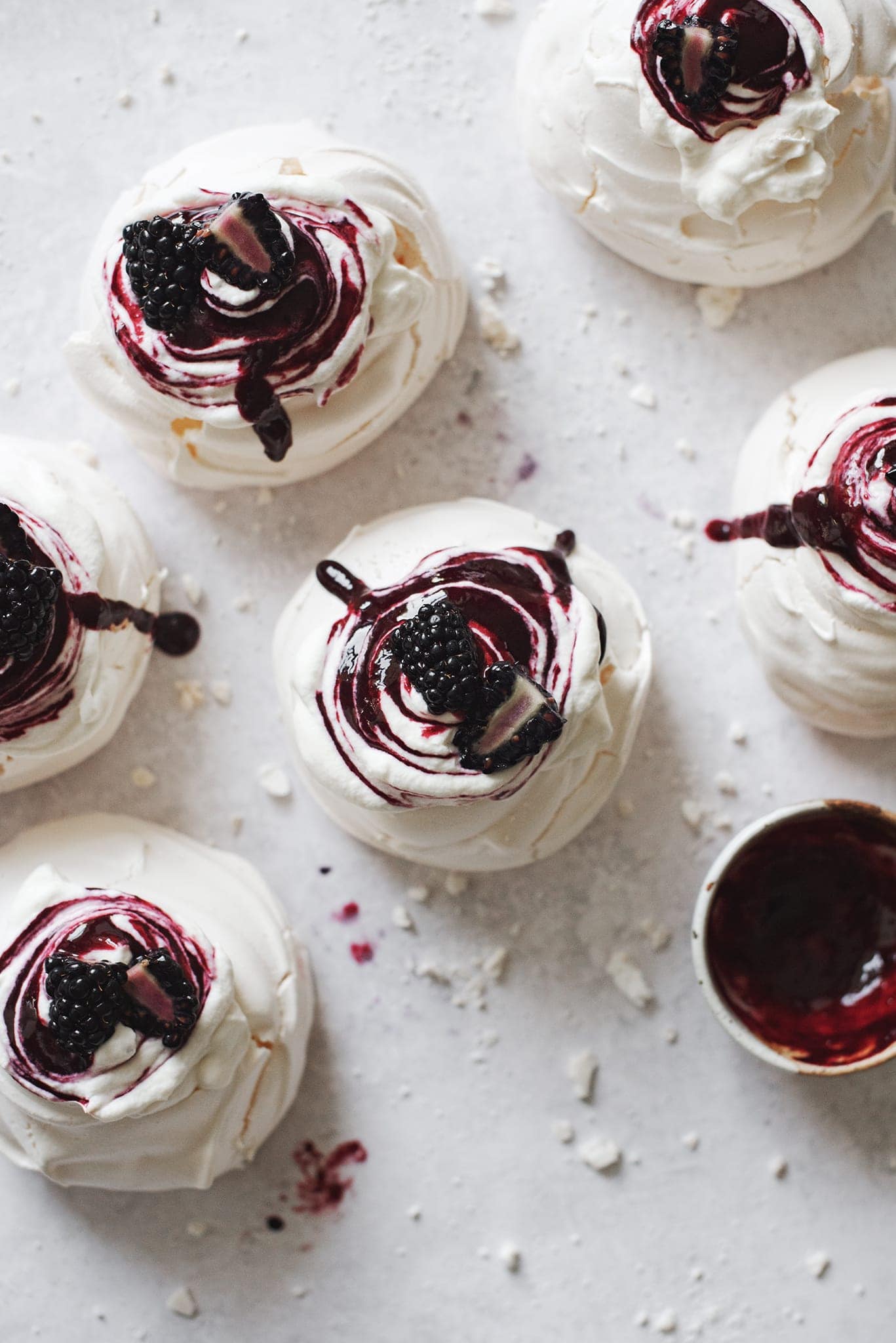 Several pavlovas topped with whipped cream, blackberry sauce, and fresh blackberries