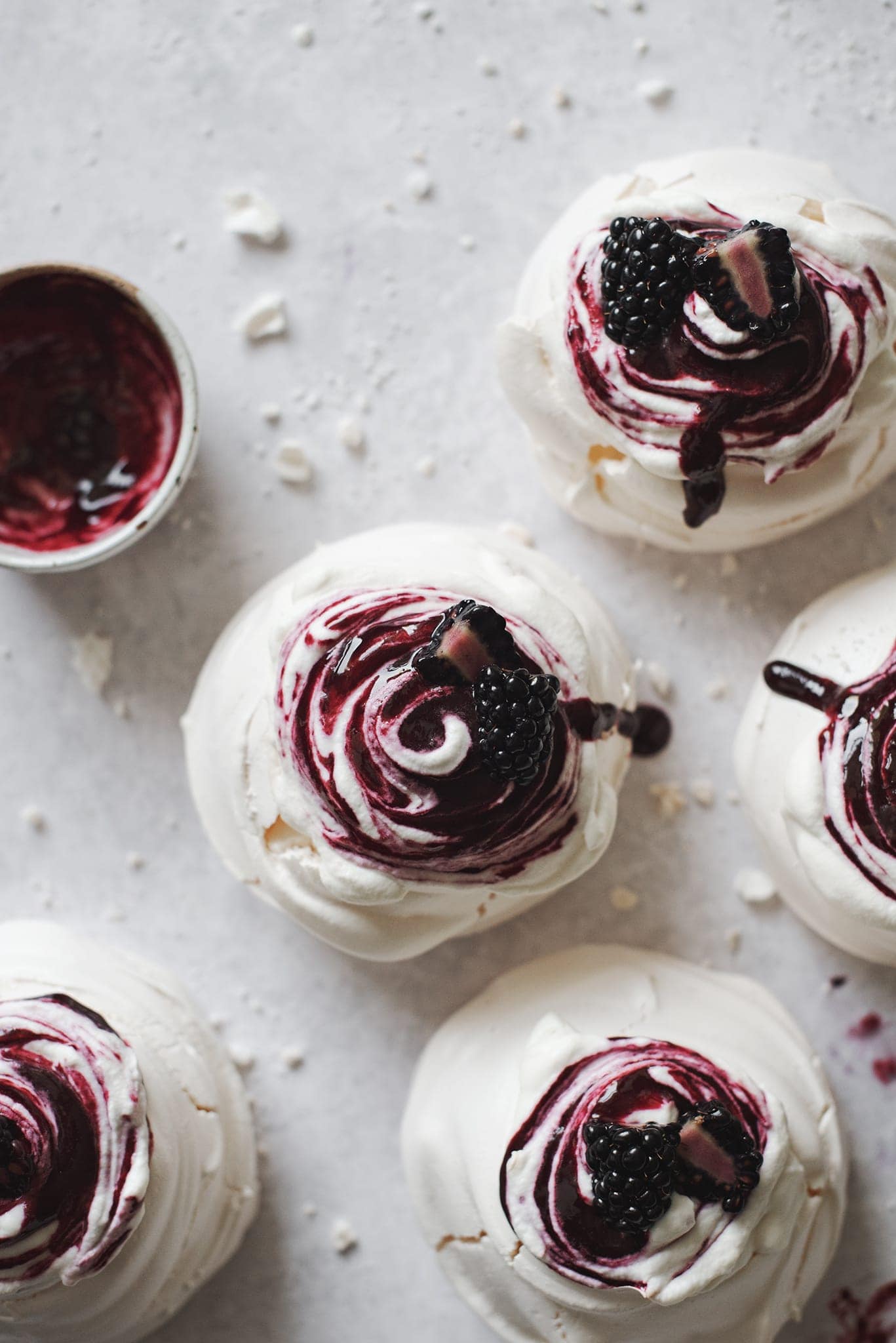 Blackberry pavlovas topped with swirls of whipped cream and blackberry sauce