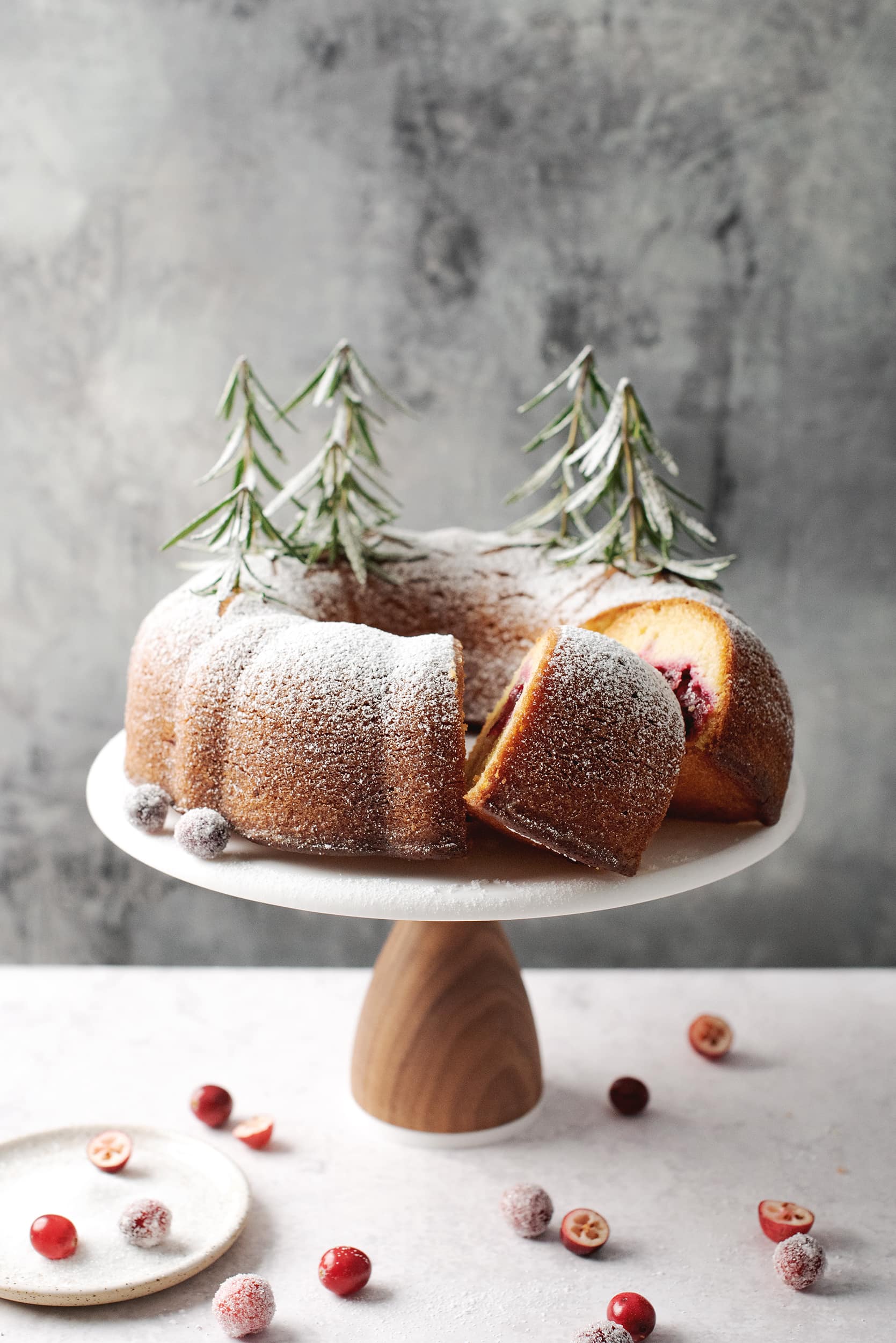 cranberry orange bundt cake with slices cut out of it on cake stand