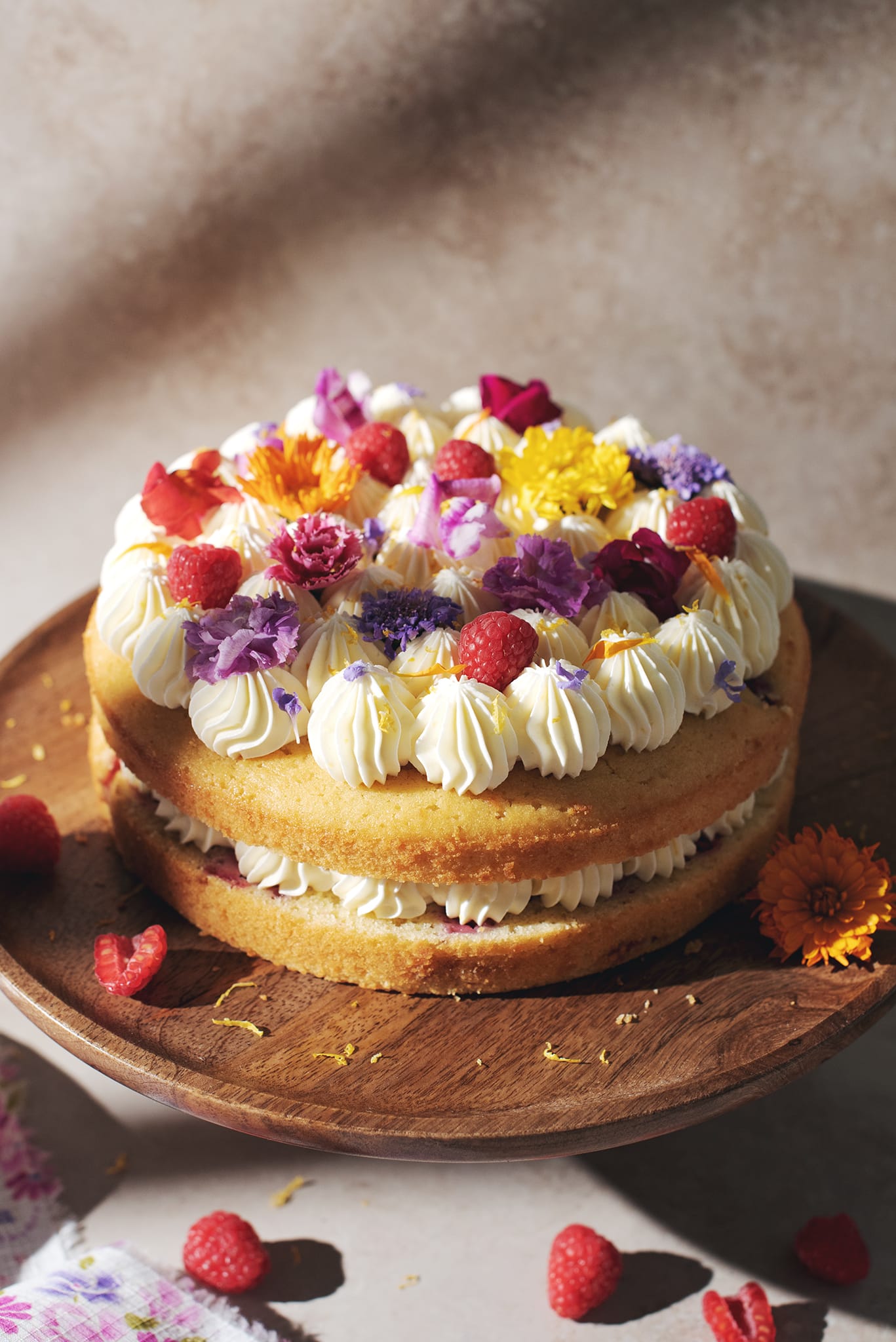 Lemon raspberry cake with layers of lemon buttercream and fresh flowers on top.