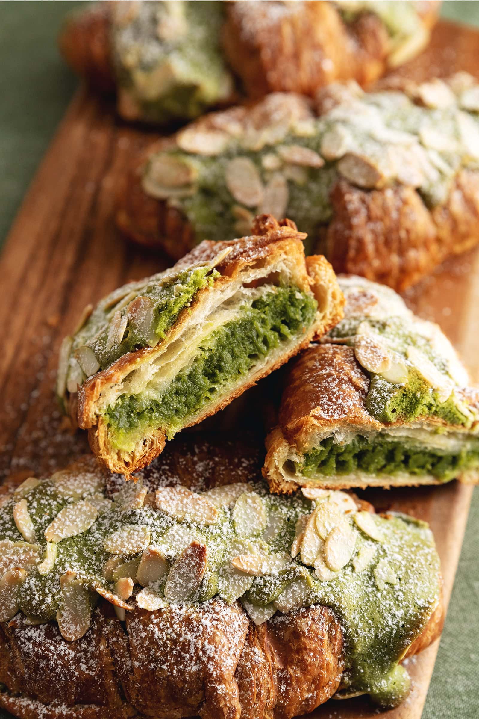 A matcha almond croissant cut in half to show the filling inside resting against other whole almond croissants.