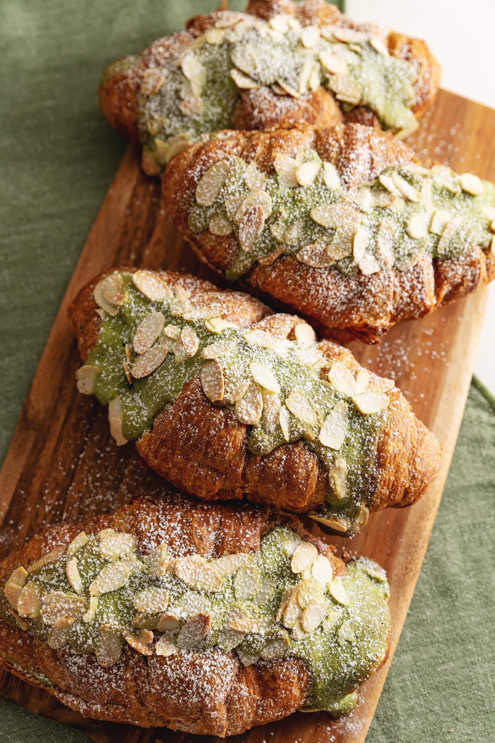 Matcha almond croissants lined up on a wooden serving board.