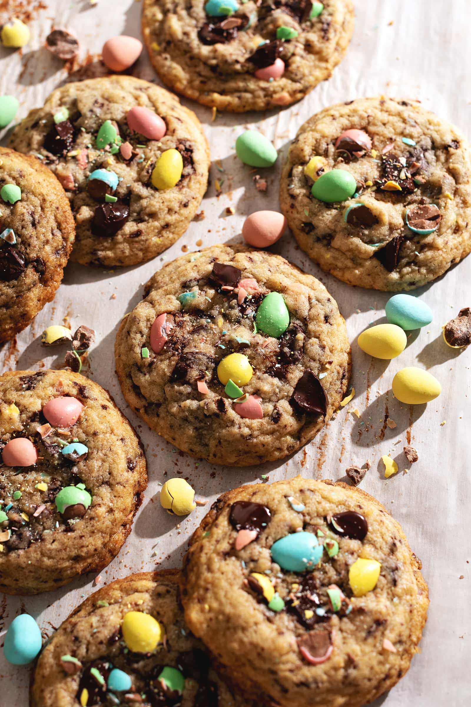Mini egg cookies scattered on parchment paper with mini egg chocolates surrounding them.