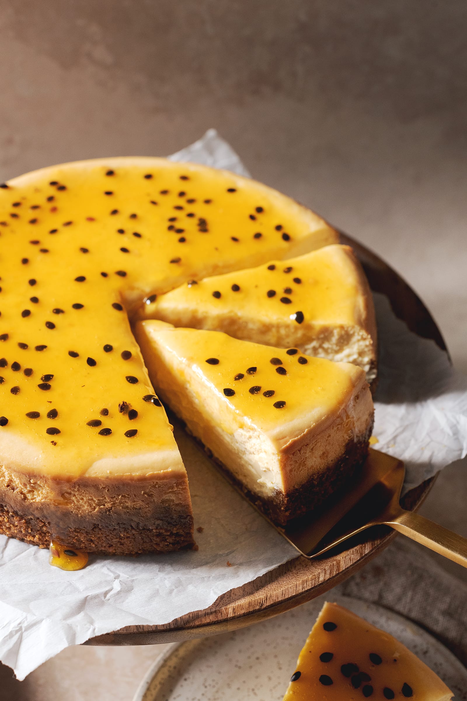 A slice of passionfruit cheesecake on a gold cake server.