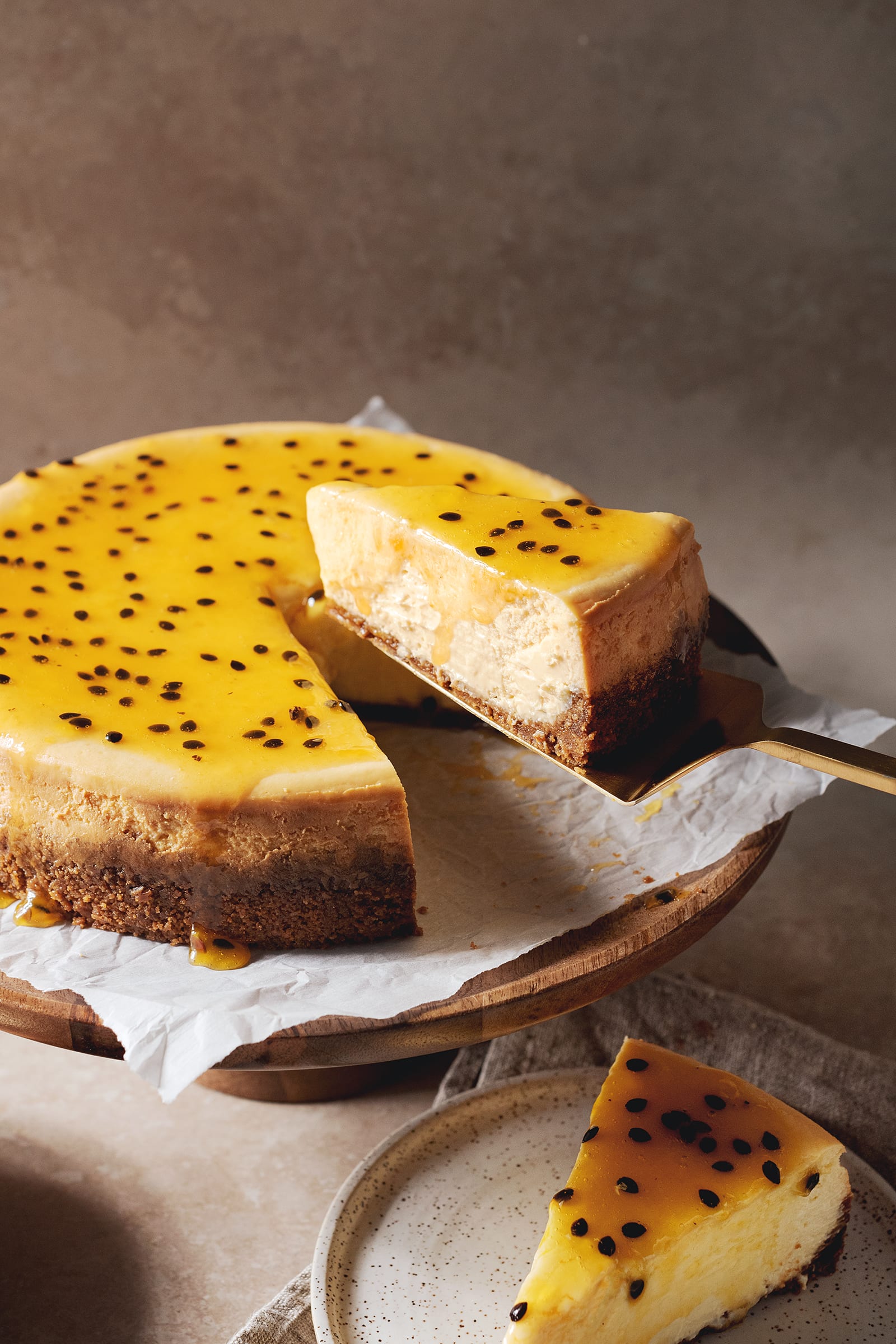 A slice of passionfruit cheesecake lifted from the cake with a gold cake server.