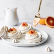 Spoonful of blood orange curd dripping into mini pavlovas
