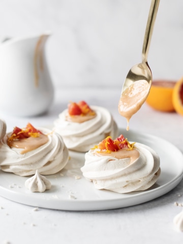 Spoonful of blood orange curd dripping into mini pavlovas