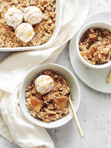 A baking dish and bowls of caramel apple crisp topped with ice cream