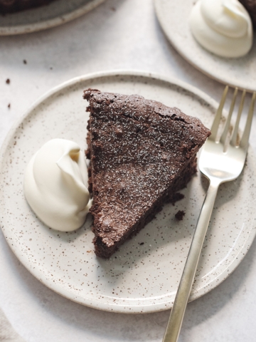 A slice of flourless chocolate cake on a plate with whipped cream