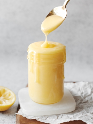Spoon dripping lemon curd into glass jar