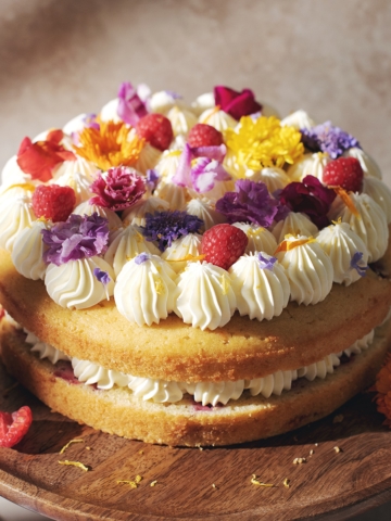 Lemon raspberry cake with layers of lemon buttercream and fresh flowers on top.