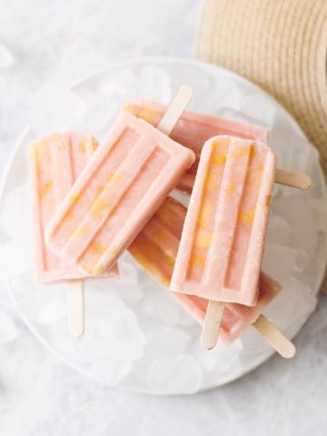 Stack of mango guava popsicles on top of plate of ice next to straw hat