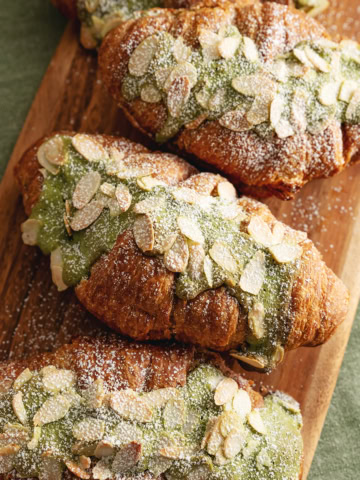 Matcha almond croissants lined up on a wooden serving board.