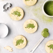 Matcha linzer cookies with triceratops cutouts on a grey background and sprinkled with matcha powder