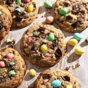 Mini egg cookies scattered on parchment paper with mini egg chocolates surrounding them.