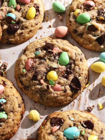 Mini egg cookies scattered on parchment paper with mini egg chocolates surrounding them.