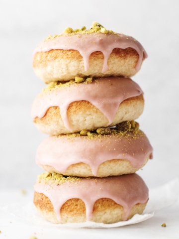Stack of four raspberry pistachio donuts dripping with glaze
